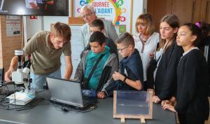 Un agent du laboratoire montre à des collégiens  quelque chose sur un ordinateur relié à un microscope