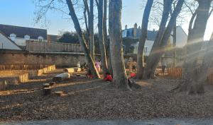 Des enfants jouent dans une zone perméable paillée de leur cour, au pied des arbres où ont été installés des jeux en bois
