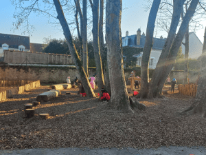 Des enfants jouent dans une zone perméable paillée de leur cour, au pied des arbres où ont été installés des jeux en bois