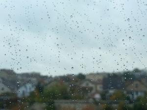 Pluie sur une vitre et ciel gris dans le deuxième plan on observe des maisons et un ciel gris