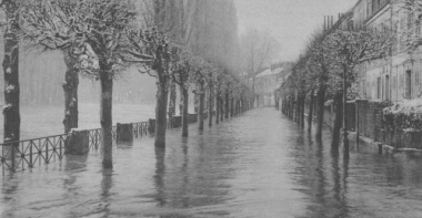 Photo en noir et blanc d'un quai arboré recouvert d'eau avec des habitations à droite.