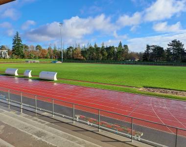 photo prise depuis les tribunes montrant un terrain en gazon naturel de bonne qualité avec la piste d'athlétisme au premier plan