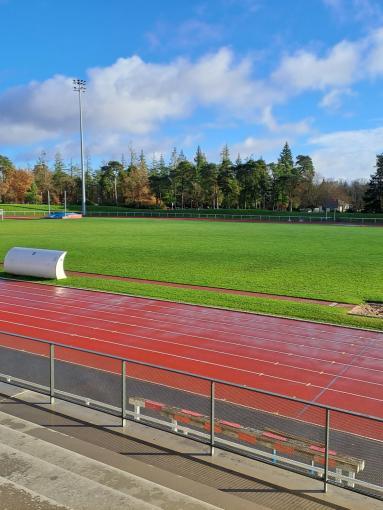 photo prise depuis les tribunes montrant un terrain en gazon naturel de bonne qualité avec la piste d'athlétisme au premier plan