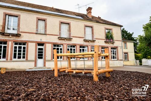 Cour d'école désimperméabilisée, avec au premier plan une passerelle d'équilibre en rondins de bois dans une zone en copeaux de bois permettant l'infiltration des eaux pluviales