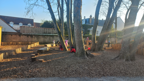 Des enfants jouent dans une zone perméable paillée de leur cour, au pied des arbres où ont été installés des jeux en bois