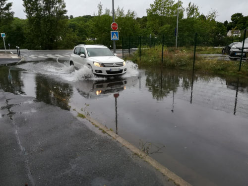 Une voiture tente de traversée une rue qui a été inondée par un débordement des réseaux d'eaux pluviales